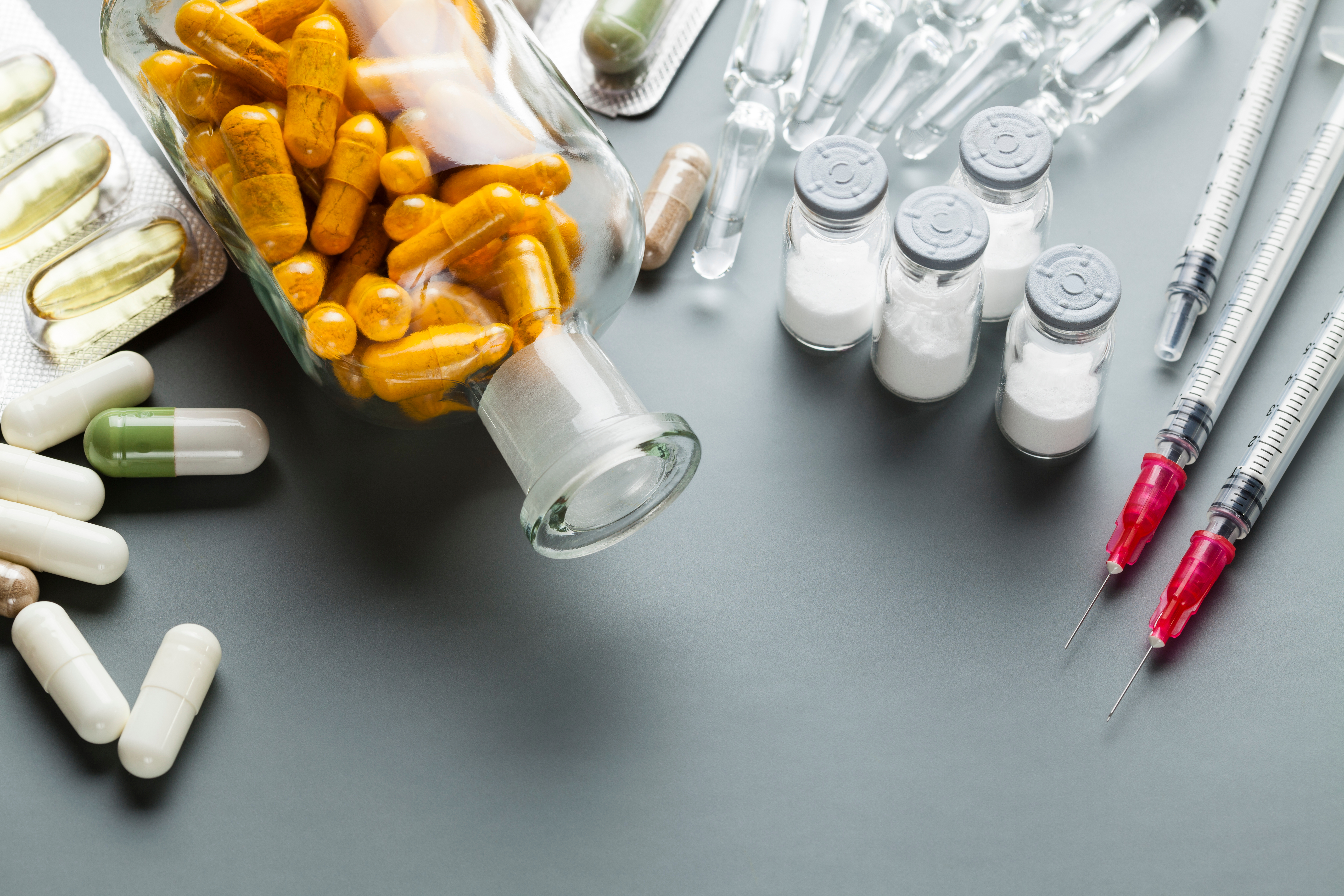 Frasco de vidro com cápsulas cor de laranja, frasco de injetáveis, ampolas, blisters, seringas.